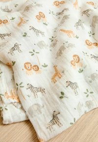 Gemusterter Musselin aus Baumwolle mit Illustrationen von Tieren wie Löwen, Elefanten und Giraffen in erdigen Tönen auf einem hellen Hintergrund.