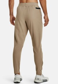 Beige sportbyxor med tapered design, elastisk midja och svart dragkedjeficka. Slät tyg med en subtil lyster.