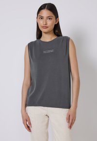 Top gris sin mangas hecho de una tela suave, con un escote redondo y el texto "NO POSPONGAS TU FELICIDAD" bordado en blanco.