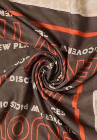 Tissu marron et beige tordu en spirale, imprimé de contours orange et de texte blanc incluant "DÉCOUVREZ DE NOUVEAUX LIEUX."