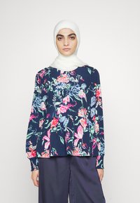 Blusa de manga longa floral em azul-marinho, com padrões vibrantes de flores rosas e verdes, de corte solto e detalhe de decote franzido.