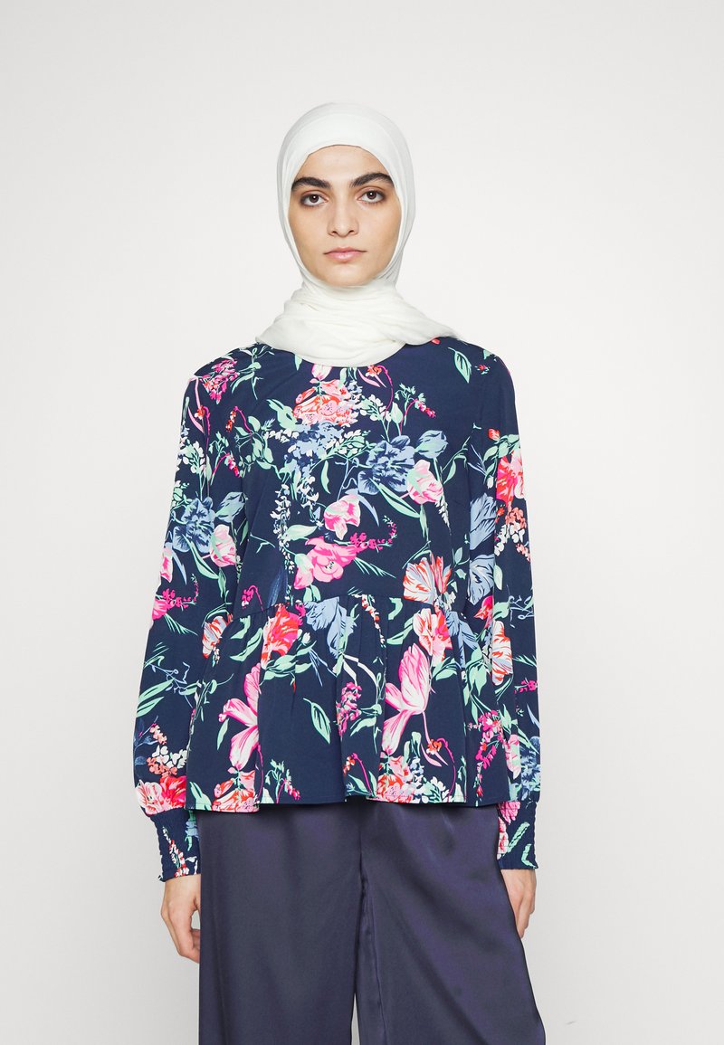 Blusa de manga longa floral em azul-marinho, com padrões vibrantes de flores rosas e verdes, de corte solto e detalhe de decote franzido.
