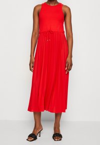 Rode mouwloze jurk met ribstructuur, strakke lijfje en geplooide rok, getailleerd met een trekkoord en voorzien van metallic accenten.