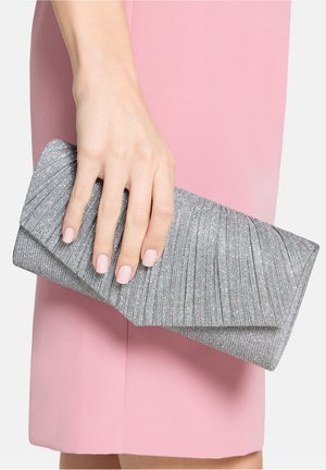 Zilveren geplooide clutch met een getextureerd oppervlak en een hoekige flapsluiting. Hand houdt de clutch vast tegen een roze jurk.