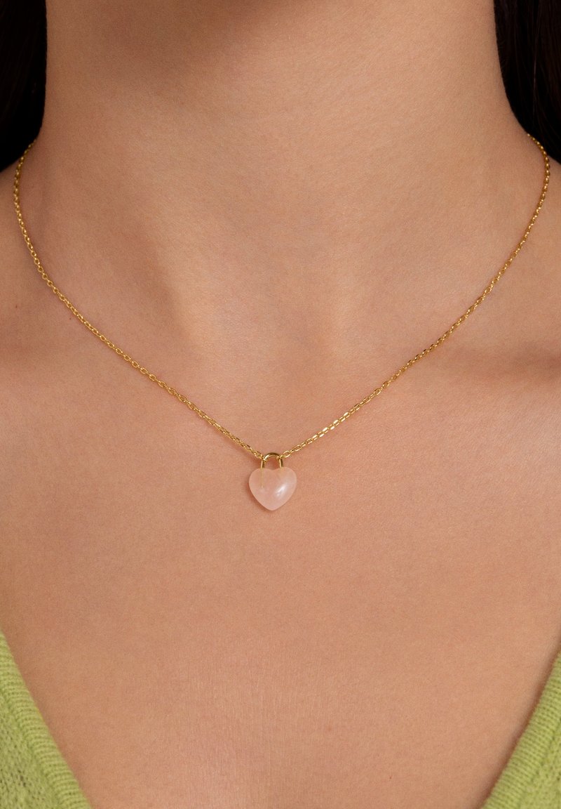 Goldene Kettenhalskette mit einem kleinen, glatten, pinkfarbenen herzförmigen Anhänger. Einfaches Design, sichtbare Gliederstruktur der Kette.