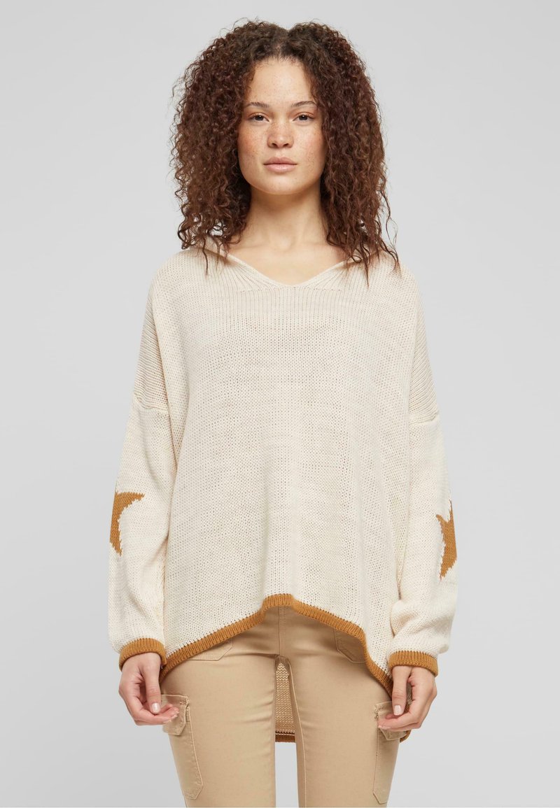 Beige knitted pullover featuring a V-neck, dropped shoulders, and brown star accents on sleeves. Hem has a contrasting brown trim.