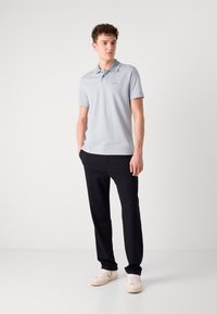 Lyseblå polo skjorte med korte ermer, med en kontrasterende krage og logo, kombinert med mørke bukser og beige sneakers.