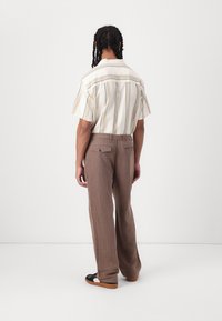 Camisa de manga corta a rayas en tonos crema y beige, combinada con pantalones de pierna ancha marrones. Los zapatos son negros con una suela marrón.