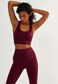Burgundowy zestaw sportowy: stanik i legginsy wykonane z oddychającego materiału, z prążkowaną teksturą i akcentami w kształcie serca na klatce piersiowej i biodrze.