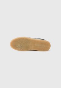 Semelle de sneaker avec un motif en caoutchouc texturé, comportant des designs en chevrons et circulaires dans des teintes de marron clair et noir.