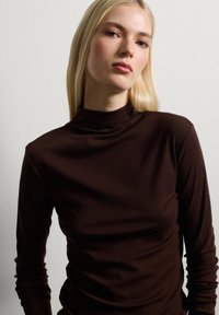 Bruine langemouwen top met een opstaande kraag, gemaakt van zachte stof met een gladde textuur en een aangesloten silhouet.