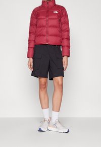 Persona vistiendo una chaqueta acolchada roja, pantalones cortos cargo negros, calcetines blancos hasta el tobillo y zapatillas de correr gris claro con acentos en azul y durazno.