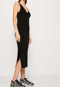 Svart ribbad stickad klänning med V-ringning, sidospalt och figursydd silhuett, kombinerad med svarta och gröna sportskor.