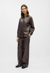 Chemise en satin marron foncé avec un col pointu, des manches longues et une fermeture à boutons, associée à un pantalon large assorti. Tissu lisse et texturé.