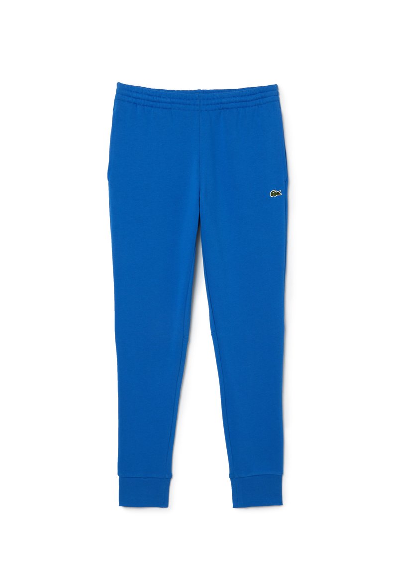 Niebieskie bawełniane dresy z elastycznym paskiem w talii i mankietami. Na lewej stronie małe zielone logo. Gładka textura, zwężający się fason.