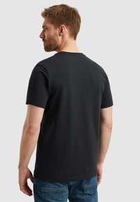 Černé bavlněné tričko s kulatým výstřihem, krátkými rukávy a rovnými lemy, v kombinaci s modrými džínami. Jednoduchý a klasický design.