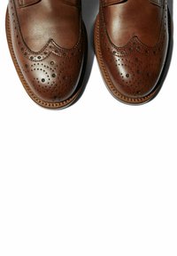 Scarpe in pelle marrone con dettagli brogue, caratterizzate da perforazioni e cuciture a bordo curvo. Texture liscia con una forma classica.
