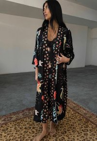 Garšs melns kimono ar krāsainiem ziedu un dzīvnieku rakstiem, ar platām piedurknēm un plūstošu dizainu. Valkāts pāri melnai mežģīņu kleitai.