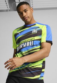 Puma atletisk t-shirt med et livligt, bølget mønster i neon grøn, blå og sort, med korte ærmer og rund halsudskæring.