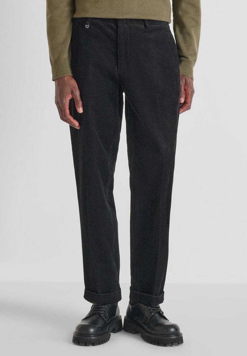 Pantaloni in corduroy neri con una vestibilità dritta, caratterizzati da una texture sottile e orli risvoltati, abbinati a scarpe nere con lacci.