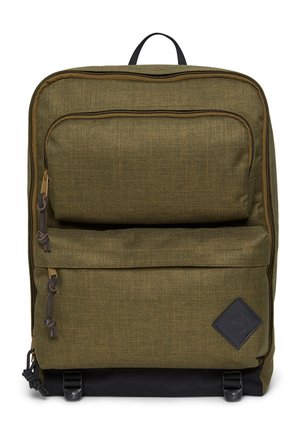 Olivgrüner Stoffrucksack mit zwei vorderen Reißverschlusstaschen, schwarzem Boden und einem schwarzen, diamantförmigen Logoaufnäher auf der unteren rechten Tasche.