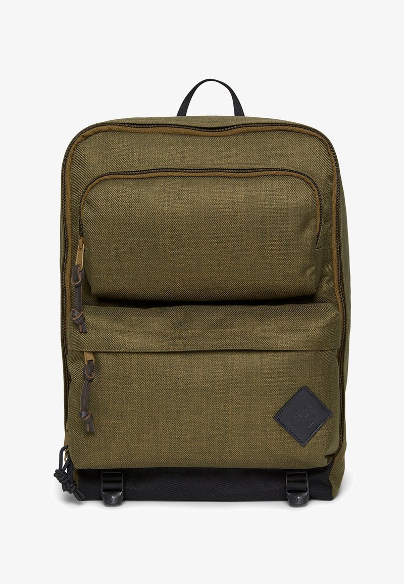 Sac à dos en tissu vert olive avec deux poches avant zippées, fond noir et un patch logo noir en forme de losange sur la poche inférieure droite.