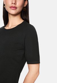 Schwarzes Kurzarmkleid mit rundem Ausschnitt, aus glattem, dehnbarem Stoff und dezenten Nähten an den Ärmeln.