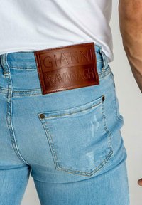 Vaqueros de denim azul claro con un prominente parche de cuero marrón en la parte posterior con texto en relieve, un ligero desvanecimiento y un diseño clásico de cinco bolsillos.