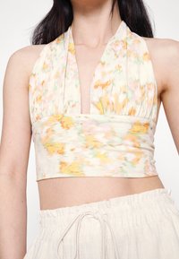 Blommönstrad crop top i pastellfärger, med halterneck-design och rynkade detaljer längs bandet. Tyget verkar mjukt och lätt.