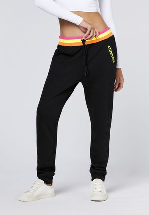 Black sweatpants with a colorful elastic waistband featuring pink, orange, and yellow stripes. Drawstring closure and logo detail on the leg.