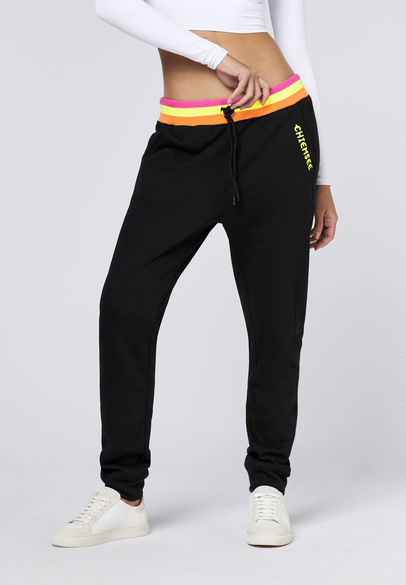 Schwarze Jogginghose mit einem bunten elastischen Bund, der rosa, orange und gelbe Streifen aufweist. Mit Kordelzugverschluss und Logodetail am Bein.