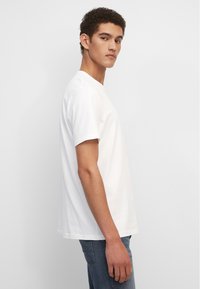 Witte katoenen t-shirt met een klassieke ronde hals en korte mouwen, met een comfortabele pasvorm en een zachte textuur. Draagt met blauwe jeans.