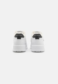 Sneakers bianchi con rivestimento in pelliccia, dettagli del logo neri sul tallone, pannelli laterali texturizzati e una suola in gomma spessa.
