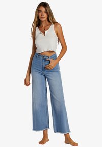 White ribbed crop top with a v-neckline paired with high-waisted light blue wide-leg jeans featuring frayed hems.