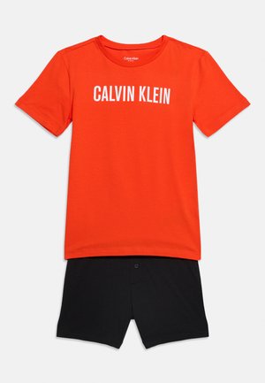 Camiseta naranja de manga corta Calvin Klein combinada con pantalones cortos negros, mostrada plana sobre un fondo claro.
