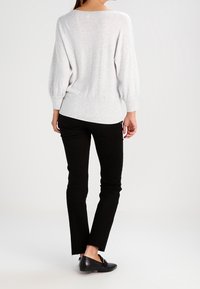Hellgrau gestrickter Pullover mit verlängerten Ärmeln und geripptem Saum, kombiniert mit schwarzen Skinny-Jeans mit ausgefransten Bündchen und flachen schwarzen Schuhen.
