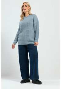 Jasnoniebieski sweter z dzianiny o luźnym kroju, okrągłym dekolcie i fakturowanym wzorze, w połączeniu z ciemnoniebieskimi dżinsami o szerokich nogawkach i czarnymi botkami na platformie.