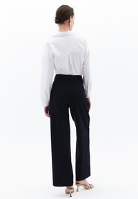 Witte blouse met kraag gecombineerd met hooggeplaatste, wijde marineblauwe broeken. Gouden bandjeshakken accentueren de outfit. Minimalistisch design en textuur.