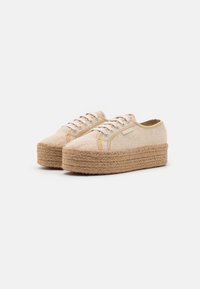 Baskets en toile à lacets avec une tige texturée beige, présentant une semelle en jute tissée épaisse et des accents jaunes subtils le long des coutures.