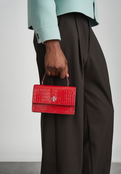 Red crocodile-embossed handbag with a top handle, silver hardware logo, and a rectangular shape, held by a hand in a mint jacket.