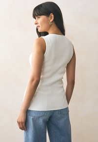 Weißes, geripptes Tanktop mit figurbetontem Schnitt, Rundhalsausschnitt und ärmellosem Design, kombiniert mit hellblauen, locker sitzenden Jeans.