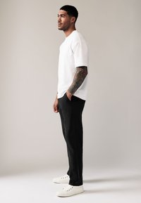 Camiseta blanca de algodón de manga corta combinada con pantalones negros y zapatillas blancas. Los pantalones tienen un corte relajado y la textura es suave.