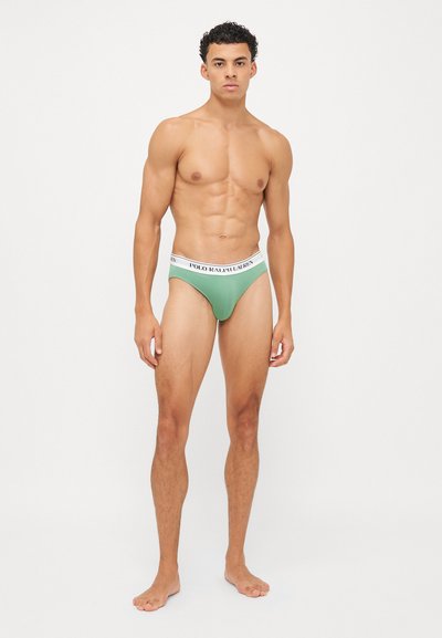 Tanga verde para hombre con una cinturilla elástica blanca que presenta la marca "POLO RALPH LAUREN" en negro. Tela suave, ajuste ceñido y diseño minimalista.
