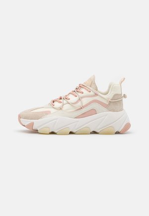 Baskets épaisses blanches et roses avec une semelle épaisse sculptée, un bout en daim, des accents roses et des lacets roses, vues de côté sur fond blanc.