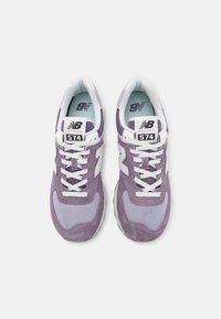 Fioletowe zamszowe i siateczkowe sneakersy z białymi akcentami, okrągłymi sznurowadłami i wyściełanym kołnierzem. Numer modelu 574 widoczny na języku.