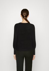 Suéter negro con un dobladillo acanalado y mangas abullonadas. Las mangas presentan embellishments de cuentas blancas, hechas de un material suave y texturizado.