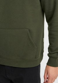 Sweat-shirt vert olive avec une poche kangourou, des poignets et un ourlet côtelés, présentant une texture douce et des détails de couture simples.
