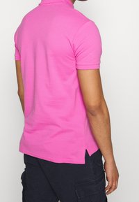 Rosa bomullspolo med kort ärm, krage och sidofickor, med en slät textur och en figursydd design.