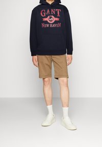 Sudadera marina con estampado rojo, bolsillo tipo canguro, combinada con pantalones cortos caqui. Zapatillas blancas y calcetines de longitud media completan el atuendo.