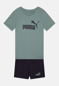 T-shirt verde in cotone con logo "PUMA" blu scuro, abbinato a pantaloni corti scuri con un logo più piccolo sull'orlo. Design semplice e casual.
